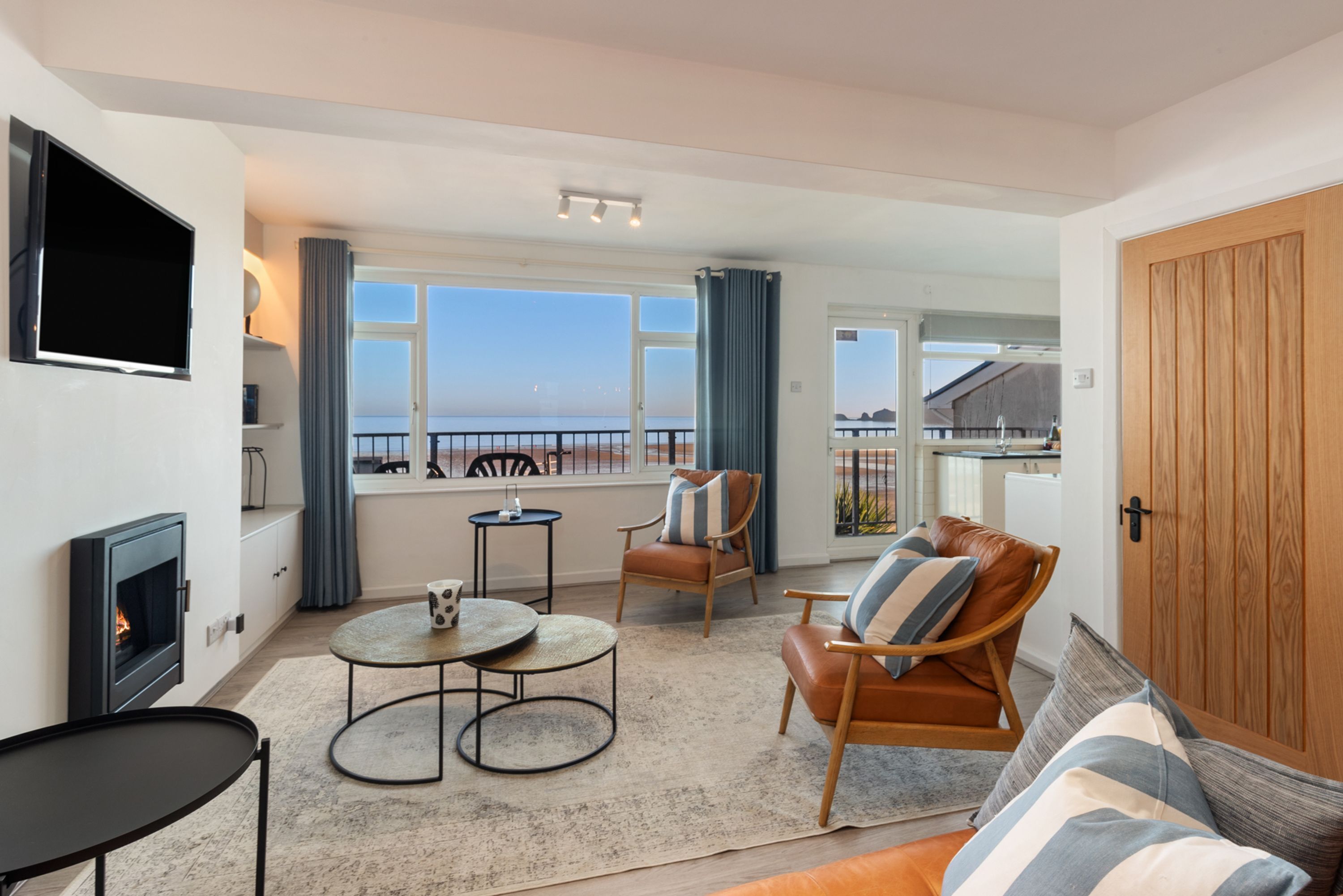 A modern living room with a fireplace, a television, and a view of the sea.