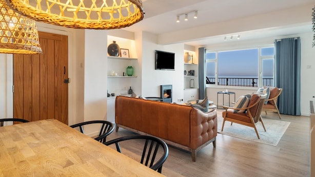 A modern living room with a fireplace, wooden furniture, and a balcony with a view. - Sea View Apartment - Sea Front Apartment With Views (Saundersfoot)