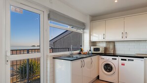 A compact kitchen with a washing machine, a microwave, and a sink. - Sea View Apartment - Sea Front Apartment With Views (Saundersfoot)