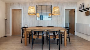 A dining area with a wooden table and chairs, pendant lights, and a mirror above the table. - Sea View Apartment - Sea Front Apartment With Views (Saundersfoot)