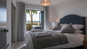 A bedroom with a bed, a nightstand, a lamp, and a view of the outdoors.