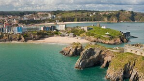 A coastal town with a prominent castle on a rocky outcrop, a sandy beach, and a mix of residential and commercial buildings.