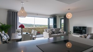 A modern living room with a large window, a flat-screen TV, and a dining area with a table and chairs.