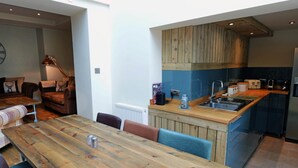 Une cuisine moderne avec des meubles en bois, un îlot central intégré doté d’un évier, et un coin repas avec une table et des chaises en bois.