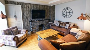 Un salon avec une cheminée en pierre, un téléviseur fixé au mur et une horloge.