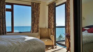 Ett hotellrum med en stor säng, en stol och en balkong med utsikt över havet.