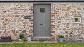 A stone building with a grey door, a sign reading "The Dairy," and two potted plants on the ground. - The Dairy - Luxury Cottage Hot Tub and Summer House Countryside Views Pet Friendly (Narberth)