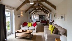 A spacious living room with high ceilings and exposed wooden beams, furnished with two sofas and a coffee table, and a kitchen in the background. - The Dairy - Luxury Cottage Hot Tub and Summer House Countryside Views Pet Friendly (Narberth)