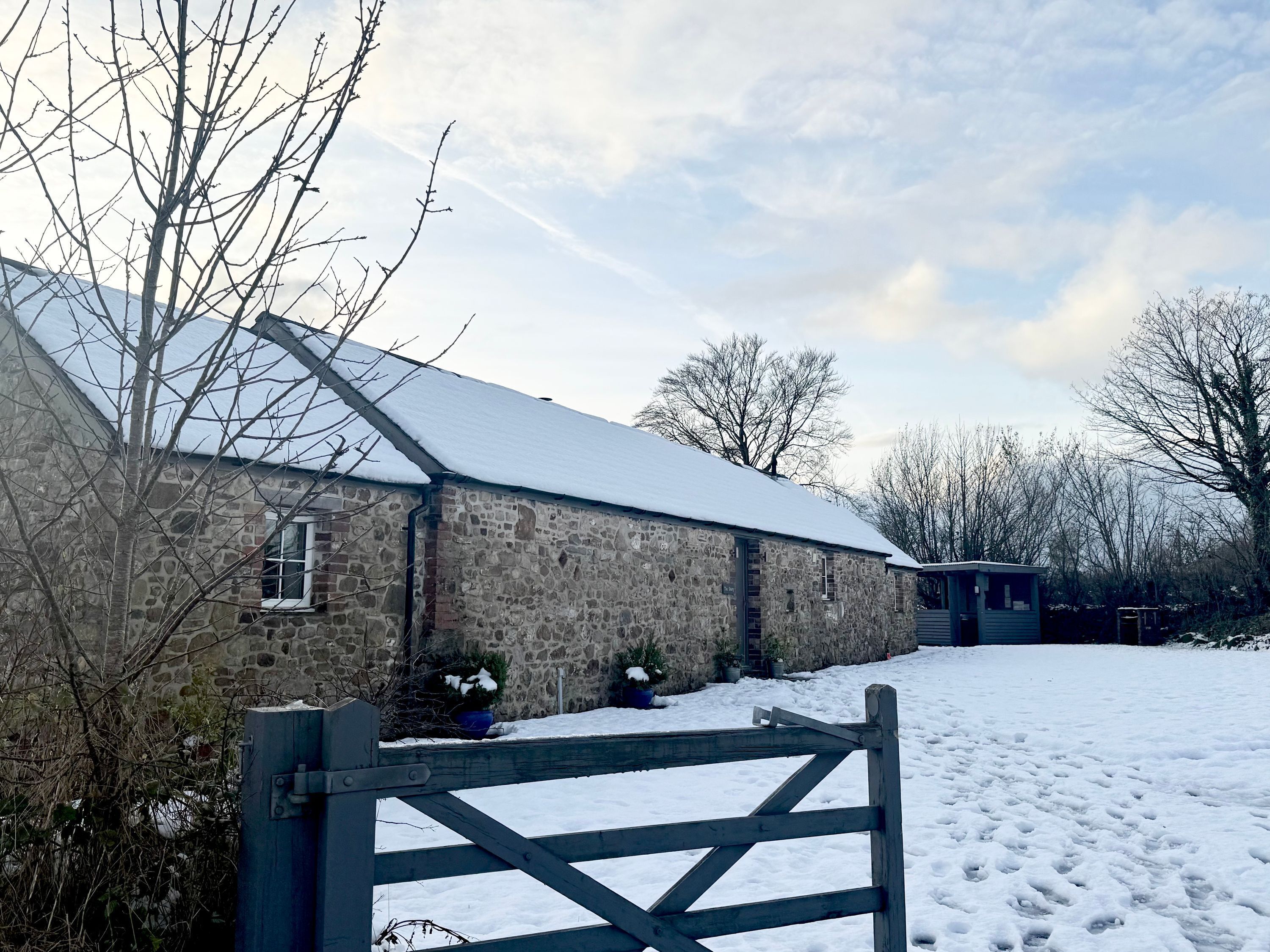 A stone building with a snow-covered roof, a wooden gate, and potted plants.