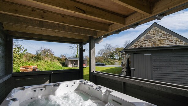 A hot tub under a wooden pergola with a stone building in the background. - The Dairy - Luxury Cottage Hot Tub and Summer House Countryside Views Pet Friendly (Narberth)