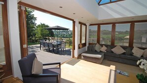 A spacious living area with a large window, a dining table with chairs, and a sofa. - Oaktree Lodge - Luxury Cottage Hot Tub Sea Views (Saundersfoot)