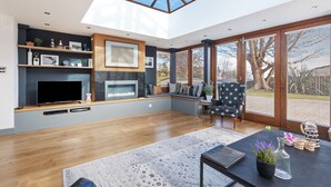 A modern living room with a built-in fireplace, a large window, and a cozy seating area. - Oaktree Lodge - Luxury Cottage Hot Tub Sea Views (Saundersfoot)