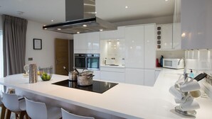 A modern kitchen with white cabinetry, a central island with a stovetop, and a microwave on the countertop. - The Hawthorns - Large Luxury Cottage Hot Tub Sea Views (Saundersfoot)