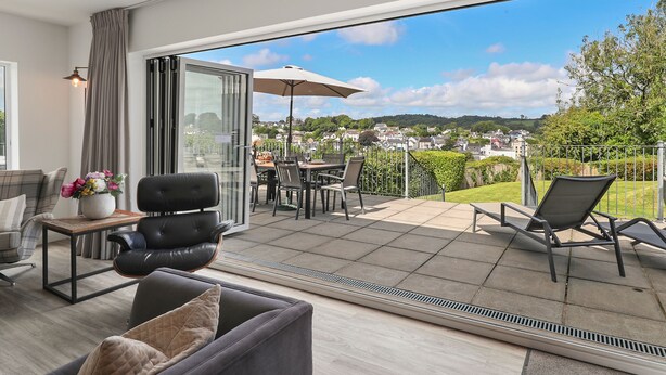 A modern living room with a sofa, armchair, and a dining area with chairs and a table. - The Hawthorns - Large Luxury Cottage Hot Tub Sea Views (Saundersfoot)