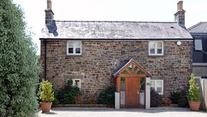 Une maison en pierre avec une porte d’entrée en bois, un petit porche et une allée pavée en briques.