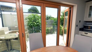 Une pièce avec une table en bois et des chaises en osier, une porte-fenêtre coulissante donnant sur une terrasse avec vue sur le jardin.
