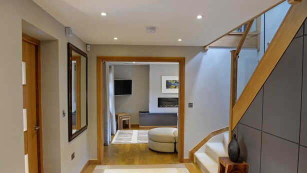 Un intérieur moderne avec un escalier en bois, un couloir menant à un espace de vie et un coin repas comprenant un canapé et un téléviseur.