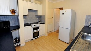 A compact kitchen with white cabinets, a black countertop, a stove, a refrigerator, and a sink. - Glan Heulog - Near to Beach Pet Friendly (Saundersfoot)