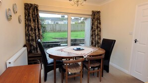 A dining area with a round wooden table, four chairs, and a chandelier. - Glan Heulog - Near to Beach Pet Friendly (Saundersfoot)
