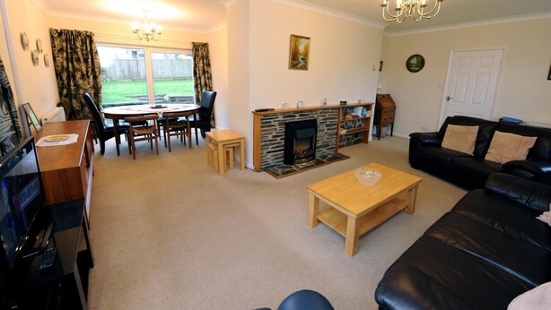 A living room with a fireplace, a dining area with a table and chairs, a black leather sofa, and a television. - Glan Heulog - Near to Beach Pet Friendly (Saundersfoot)
