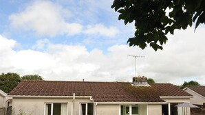 A two-story house with a tiled roof, a satellite dish, and a small garden with a lawn and a bush. - Glan Heulog - Near to Beach Pet Friendly (Saundersfoot)