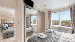 A bedroom with a large bed, a TV, and a view of the countryside. - Valley View Lodge - Luxury Lodge Hot Tub Close to Beach (Tenby)