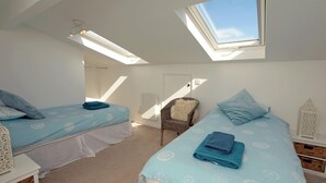 Ein Schlafzimmer mit zwei Betten, einem Oberlicht und einem Korbstuhl.