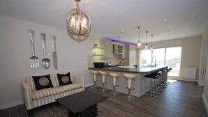 A modern kitchen with a central island, bar stools, and a dining area with a sofa. - Amber Cottage - Luxury Cottage Hot Tub Sea Views and Log Burner (Saundersfoot)