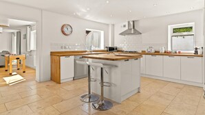 A modern kitchen with a central island, white cabinetry, and a wooden countertop. - Am Byth - Luxury Cottage Sea Views (Saundersfoot)