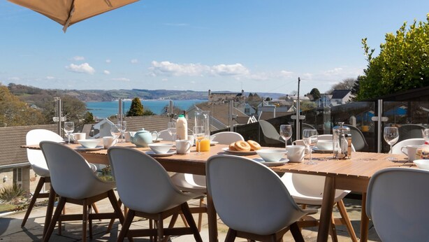 An outdoor dining area with a table set for four, overlooking a scenic coastal view. - Am Byth - Luxury Cottage Sea Views (Saundersfoot)