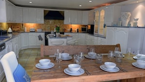A modern kitchen with white cabinetry, a central island, and a dining table set for six. - Swallow Dale - Large Pet Friendly Cottage (Saundersfoot)