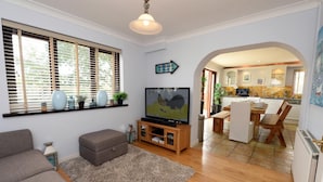 A living room with a TV, sofa, and a dining area with chairs and a table. - Swallow Dale - Large Pet Friendly Cottage (Saundersfoot)