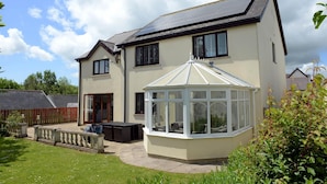A two-story house with a conservatory, a fenced garden, and a sloped roof. - Swallow Dale - Large Pet Friendly Cottage (Saundersfoot)