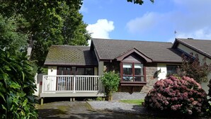 A two-story house with a stone facade, a small porch, and a large bush in the front yard.