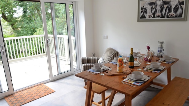 A dining area with a wooden table set for four, a bench, and a view of a balcony with a white railing.