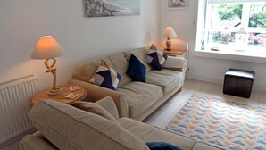 A living room with a beige sofa set, two side tables with lamps, a patterned rug, and a window with a view of greenery.