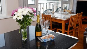 A dining table set with a bottle of champagne, glasses, and a box of pastries.