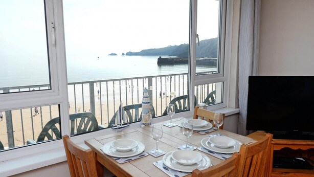 A dining table set for four with a view of the sea and a lighthouse through large windows.