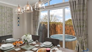 Un coin repas avec une table dressée pour deux personnes, un jacuzzi et une vue sur une clôture en bois et des arbres.