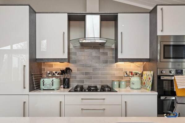 A modern kitchen with white cabinets, a gas stove, a microwave, and a toaster. - Trevelyn Lodge - Luxury Lodge Hot Tub Close to Beach (Tenby)