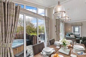A dining area with a hot tub, a table set for a meal, and a view of the outdoors. - Trevelyn Lodge - Luxury Lodge Hot Tub Close to Beach (Tenby)