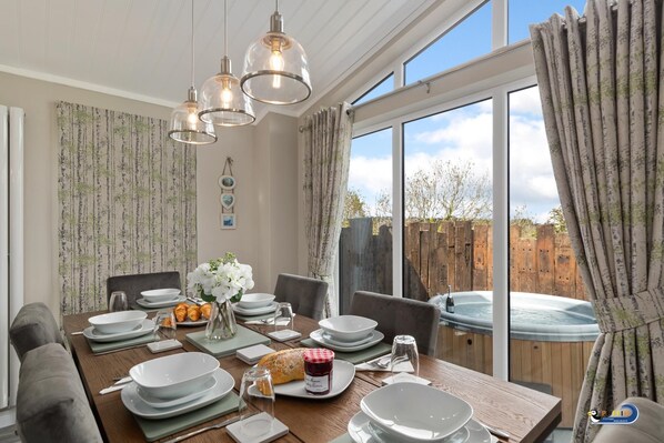 Enjoy meals in this stylish dining area with a large table for four, adjacent to a window offering a view of a deck and hot tub.
