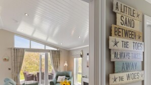 Une pièce avec une grande fenêtre, un fauteuil vert et un mur orné d’une plaque en bois sur laquelle on peut lire : « Un peu de sable entre les orteils, et tous les soucis s’envolent. »
