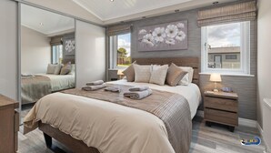 Une chambre à coucher moderne avec un grand lit, une table de chevet, un miroir et une fenêtre avec des rideaux.