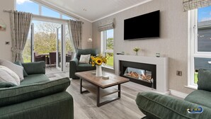 Un salon moderne doté d’une cheminée, de canapés verts, d’une table basse ornée d’un vase de tournesols et d’un téléviseur à écran plat fixé au mur.