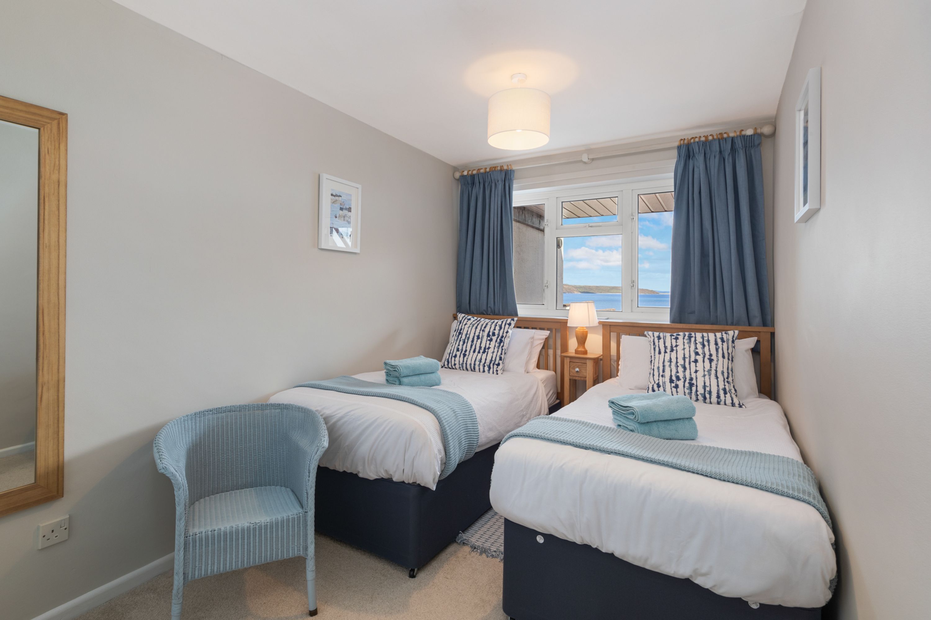 A bedroom with two beds, a chair, a nightstand, and a window with curtains.