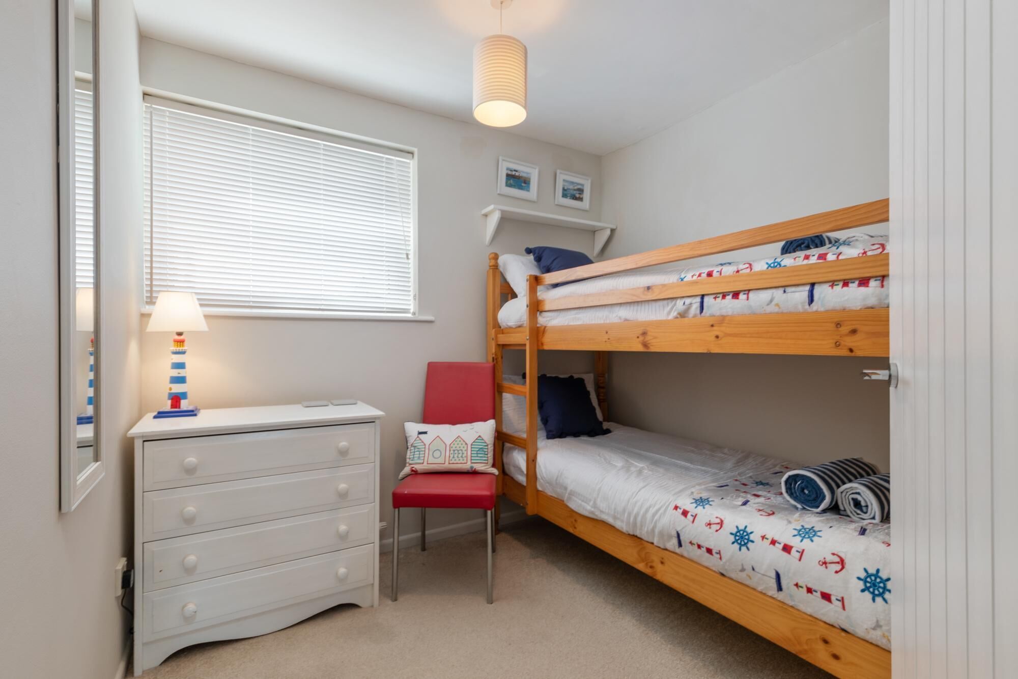 Een slaapkamer met een stapelbed, bureau, stoel en lamp.
