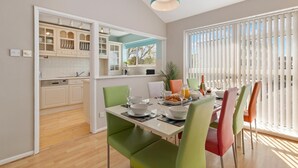 A modern kitchen with white cabinets and a dining area with colorful chairs. - Cystanog Fach - Spectacular Sea Views Balcony and Terrace Parking (Saundersfoot)