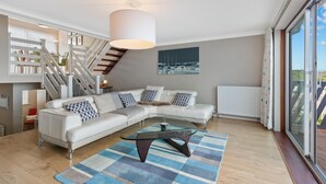 A modern living room with a white sectional sofa, a glass coffee table, and a staircase with white railings. - Cystanog Fach - Spectacular Sea Views Balcony and Terrace Parking (Saundersfoot)