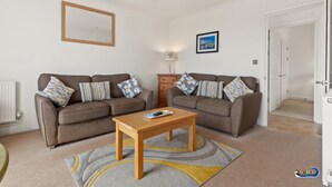 Ein Wohnzimmer mit zwei Sofas, einem Holztisch, einer Lampe und einem gerahmten Bild an der Wand.